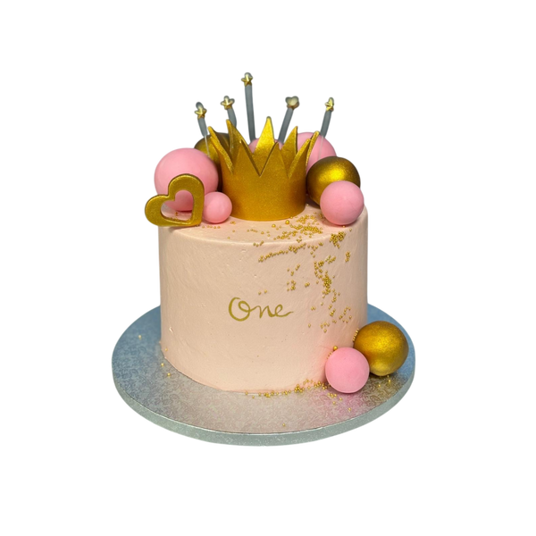 Rosa Geburtstagstorte mit goldener Krone, pinken und goldenen Kugeln sowie der Aufschrift „One“ für den 1. Geburtstag. Edles und märchenhaftes Design mit glänzenden Gold-Akzenten