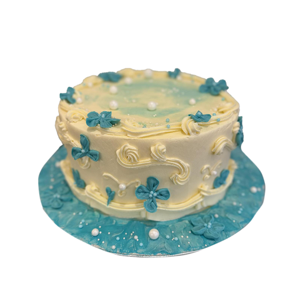 Weiße Torte mit blauen gespritzten Blumen, Perlen und weißer Spritzdeko