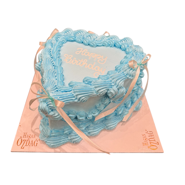 herzförmige Torte in Himmelblau, dekoriert mit feiner Buttercreme in Rüschenoptik und zarten Schleifen. Verziert mit der Botschaft 'Happy Birthday'. Perfekt für Geburtstage und elegante Anlässe."
