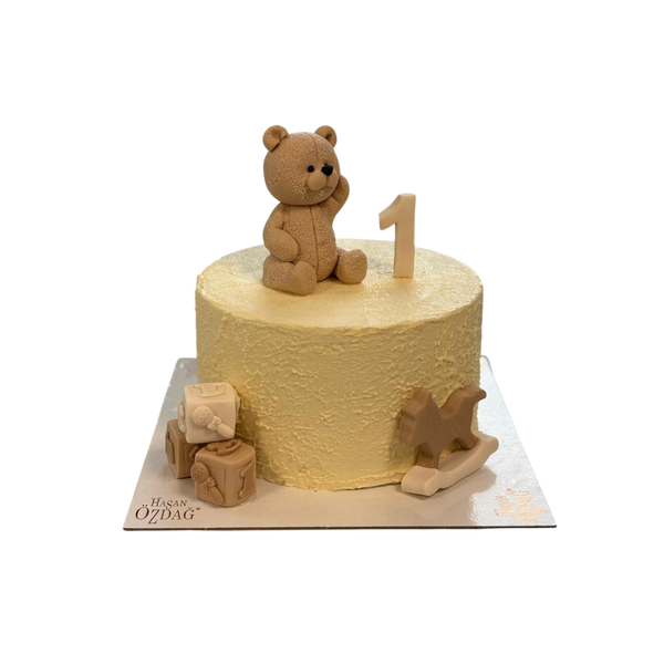 "Kindergeburtstagstorte mit zarter Buttercreme, dekoriert mit einem handmodellierten Teddybär, einem Schaukelpferd, Würfeln und der Zahl 1. Perfekt für den ersten Geburtstag oder kindliche Anlässe."