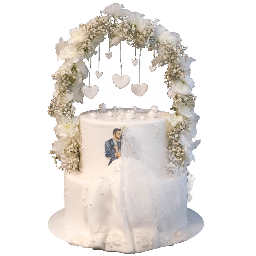 Weiße zweistöckige Hochzeitstorte mit Blumen-Bogen, an dem Herzen hängen.  Vorne ist eine Brautpaar-Illustration mit 3D-Kleid aus Fondant. Die Torte ist mit Perlen dekoriert.