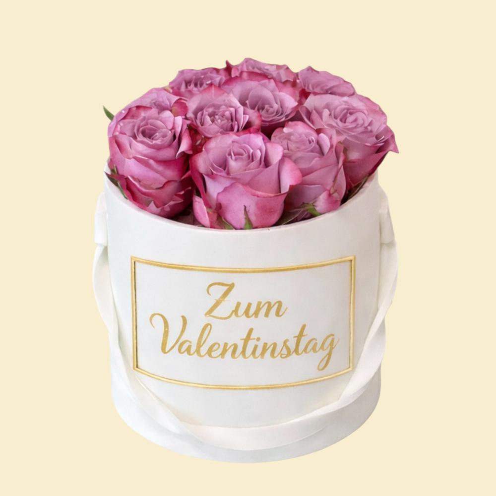 Runde weiße Torte im eleganten Stil, gefüllt mit rosafarbenen Rosen und verziert mit einer goldenen Aufschrift „Zum Valentinstag“ auf der Vorderseite; präsentiert vor hellem Hintergrund.
