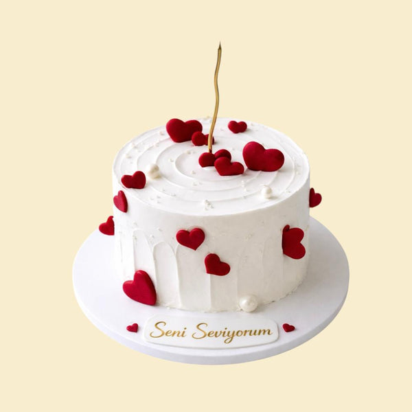 Weiße, runde Torte mit glatter Creme Oberfläche, dekoriert mit roten Herzen und Perlen