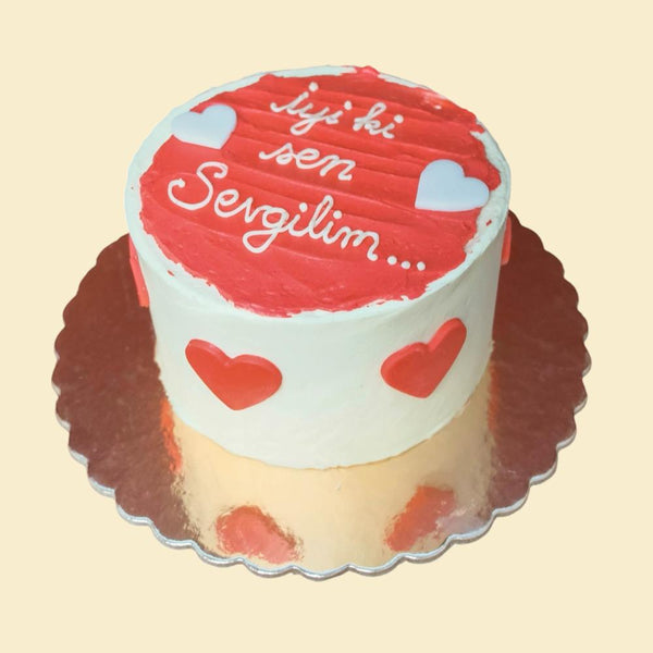 Runde Liebestorte in Weiß und Rot mit Herzmotiven und der Aufschrift „İyi ki sen Sevgilim“ auf glänzender goldener Tortenplatte.