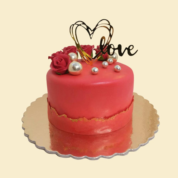 Runde, rote Torte mit matter Oberfläche, goldener Akzentlinie, roten Rosen, silbernen Perlen und Herz-Topper mit Schriftzug „love“.