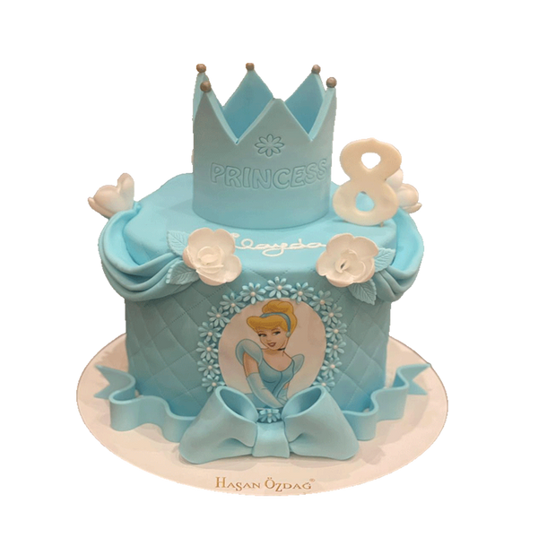 Das Bild zeigt eine elegante, einstöckige Geburtstagstorte im Cinderella-Prinzessinnen-Stil. Die Torte ist in einem hellen Blauton gehalten und mit einem Rautenmuster verziert. Auf der Vorderseite befindet sich ein Bild von Cinderella, umgeben von blauen und weißen Zuckergussblumen. Oben auf der Torte steht eine große, blaue Krone . Die Torte wird von Zuckergussrosen und einer großen Schleife am unteren Rand