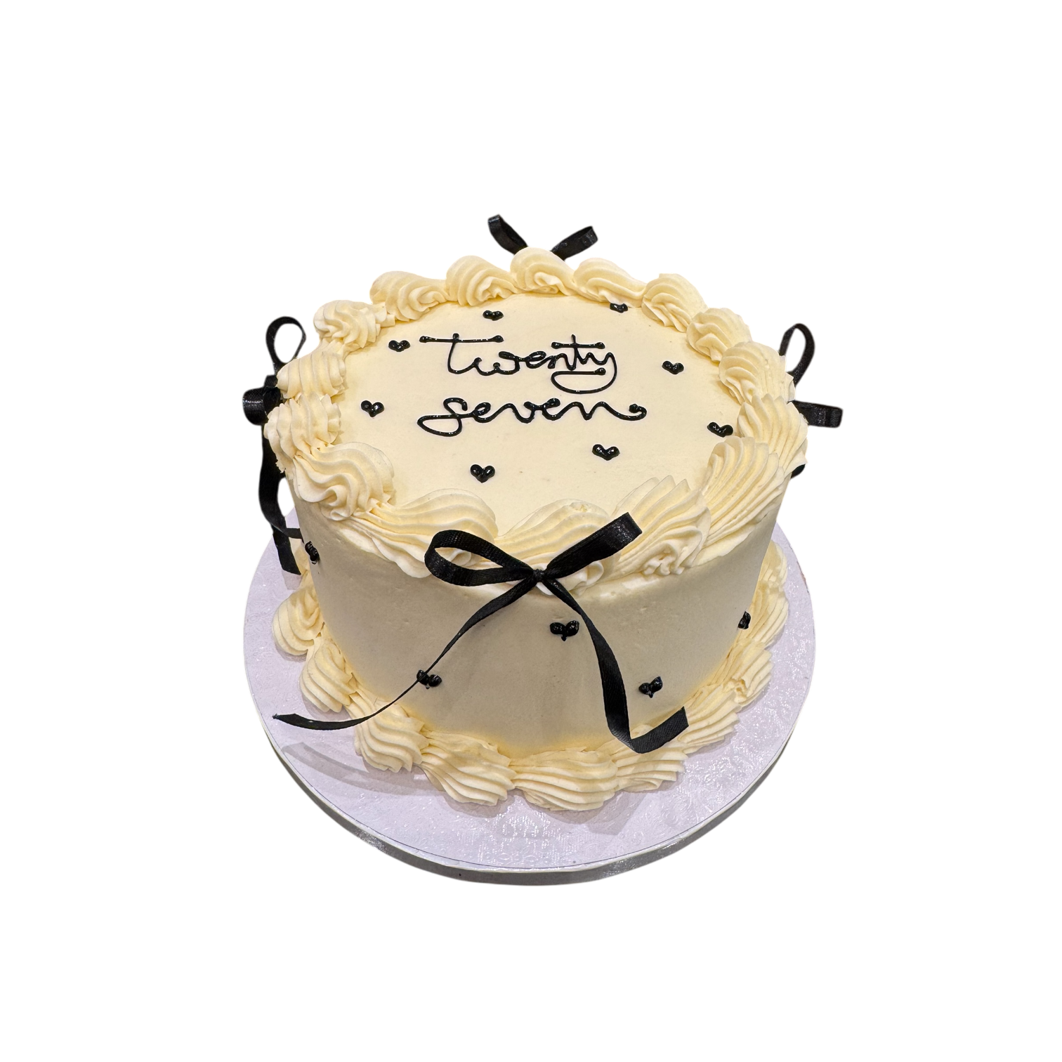 Elegante weiße Sahnetorte mit handschriftlichem Schriftzug „Twenty Seven“, dekoriert mit schwarzen Schleifen und filigranen Sahneverzierungen