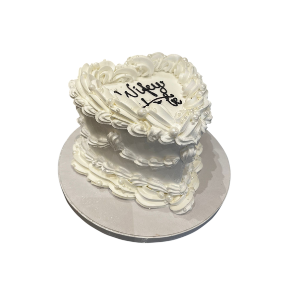 herzförmige Torte mit weißer Verzierung, Perlendetails und der Aufschrift „Wifey to be“ 